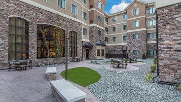 A courtyard with outdoor seating, a stone wall, and a building with multiple windows.