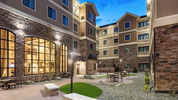 Un patio de hotel con muros de piedra, ventanas amplias, mobiliario exterior y un ambiente luminoso.