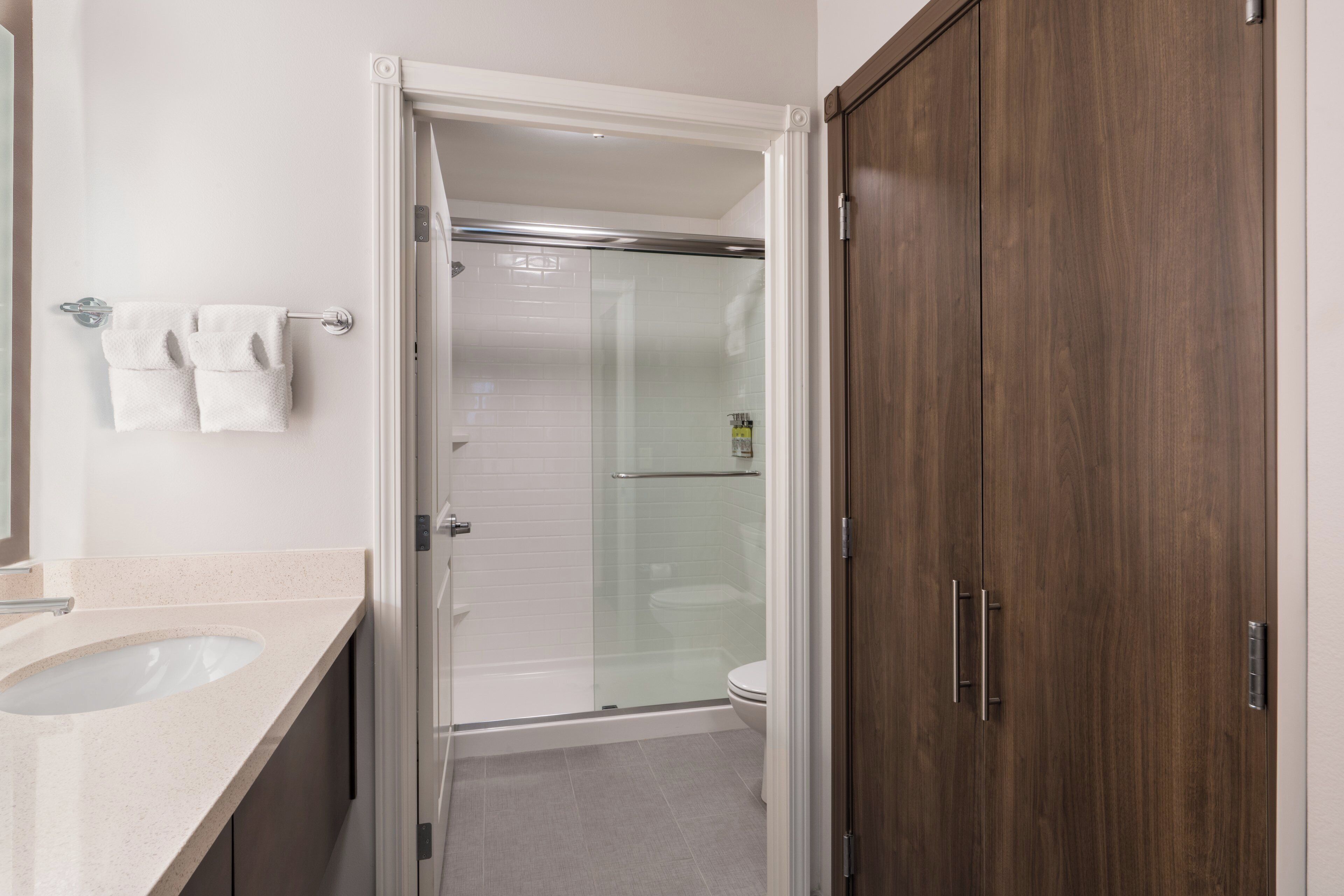 A bathroom with a glass-enclosed shower, a white sink, and a wooden wardrobe.