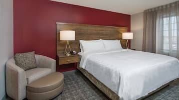 A hotel room with a large bed, two bedside lamps, a wooden headboard, a beige armchair, and a small table with a telephone.