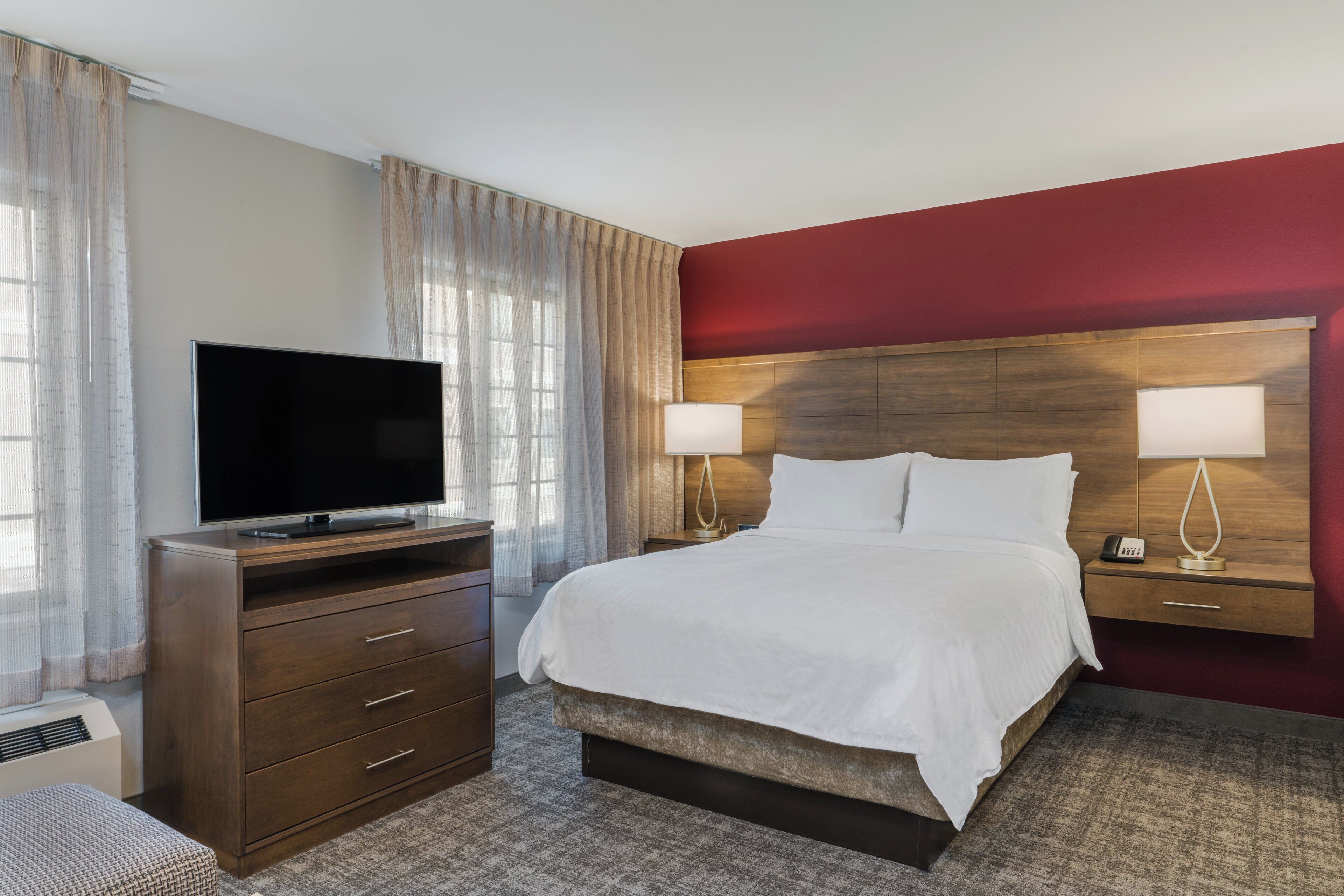 A hotel room with a bed, a TV, a dresser, and a nightstand with lamps.