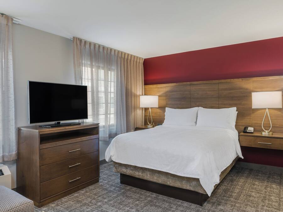 A hotel room with a bed, a TV, a dresser, and a nightstand with lamps.