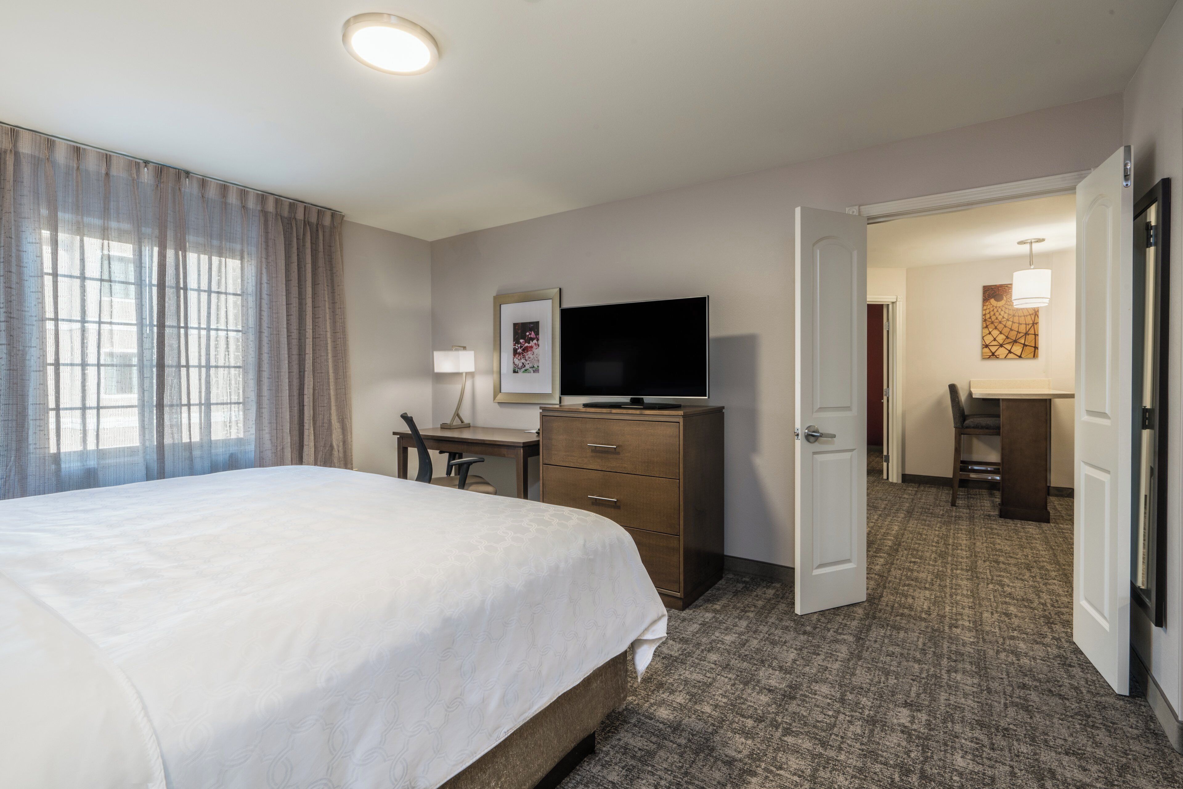 A hotel room with a bed, desk, television, and a door leading to another room.