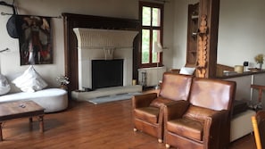 A living room with a fireplace, leather armchair, sofa, and wooden flooring.