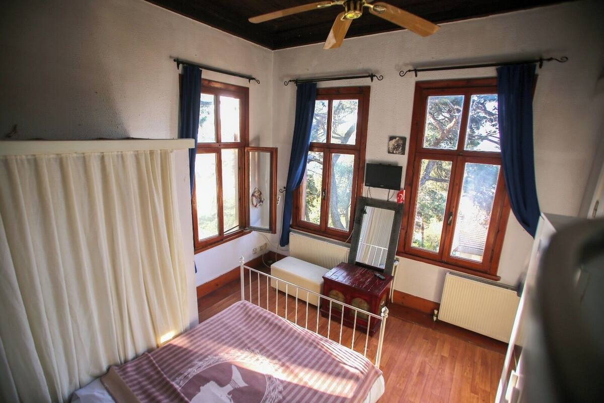 Ein Schlafzimmer mit einem Bett, einem hölzernen Deckenventilator, einem Fenster mit Vorhängen und einer Heizung.