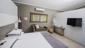 Ein modernes Hotelzimmer mit Bett, Sitzecke, Sessel, Fernseher und einem Fenster mit Jalousien.