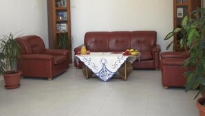 Un salon avec un canapé en cuir marron, une table basse recouverte d’une nappe blanche et deux étagères en bois.