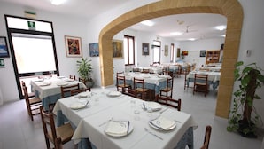 Un espace repas avec des tables disposées pour accueillir plusieurs personnes, agrémenté d’une arche en briques, de murs blancs et de diverses œuvres d’art.