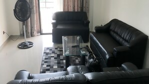 A living room with a black leather sofa, a glass coffee table, and a standing fan.
