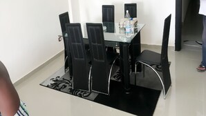 A dining area with a glass table, black chairs, and a black rug.
