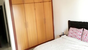 A bedroom with a large wardrobe, a bed with floral bedding, and a nightstand.