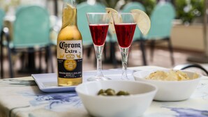 A table with a bottle of Corona Extra, two glasses of red beverage, a bowl of olives, and a plate of chips. - Hotel Belmar (Rimini)