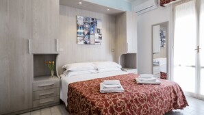 A hotel room with a bed, a nightstand, a mirror, and a wall-mounted air conditioning unit. - Hotel Belmar (Rimini)