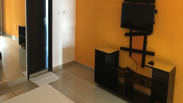 Een moderne kamer met een zwarte deur, een aan de muur bevestigde televisie en een betegelde vloer.
