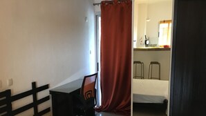 Een slaapkamer met een bed, een bureau en een stoel. Een badkamer is zichtbaar door een open deur.