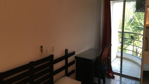 Een kamer met een bed, een bureau en een stoel. Er is een raam met gordijnen, en uitzicht op palmbomen.
