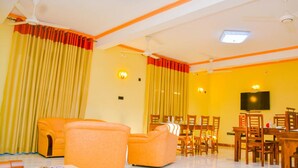 A room with orange sofas, a dining table with chairs, a flat-screen TV mounted on the wall, and ceiling fans. - Marathona Tourist Resort - Anuradhapura (Anuradhapura)