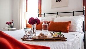 A neatly made bed with white linens, a tray of cookies, a glass of water, and a bottle of wine on a bedside table. - Aika Hotel Alaybey (Bozcaada)