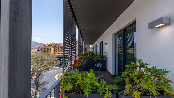 A balcony with potted plants, a view of a cityscape, and a building with a modern design.
