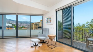 A spacious balcony with a city view, a grey armchair, a small wooden table, and a white ottoman.