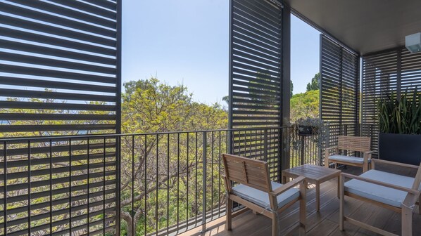 A balcony with a wooden bench, a small table, and a chair.