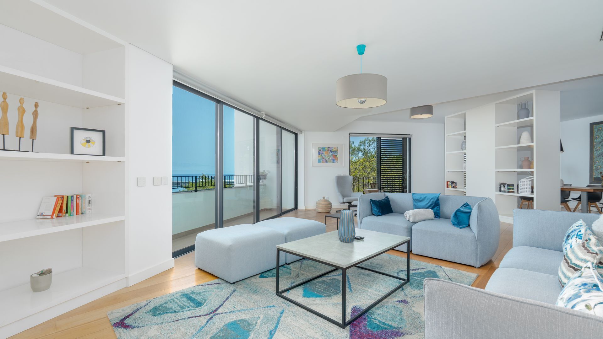 Una sala de estar moderna con un ventanal grande, un sofá, una mesa de centro y una estantería.