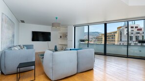 Un salon moderne doté d’un téléviseur à écran plat, de canapés gris, d’une petite table et d’une grande fenêtre offrant une vue sur la ville.