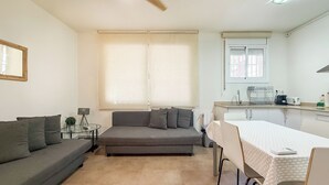 Espaço compacto com sofá, mesa de jantar, pequena cozinha e ventilador de teto.
