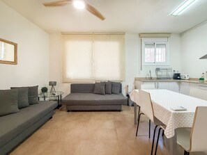 Un espace de vie compact comprenant un canapé, une table à manger, un petit coin cuisine et un ventilateur de plafond.