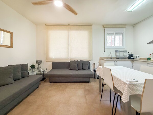 A compact living space with a sofa, a dining table, a small kitchen area, and a ceiling fan.