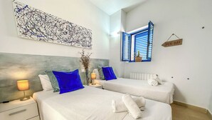 Une chambre d’hôtel avec deux lits, une grande peinture abstraite, une fenêtre avec des volets bleus et un panneau indiquant qu’un bar est ouvert.