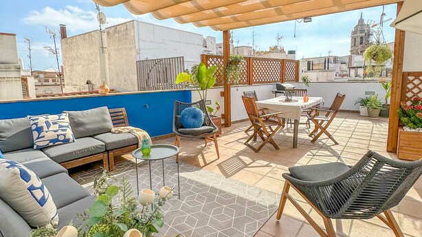 Une terrasse sur le toit dotée d’un espace salon couvert, d’une table à manger et de diverses plantes.