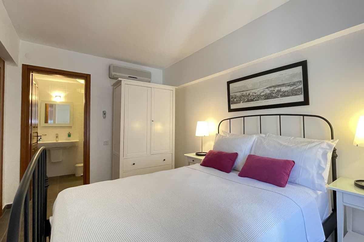 A bedroom with a bed, two bedside tables with lamps, a wardrobe, and a framed picture on the wall.