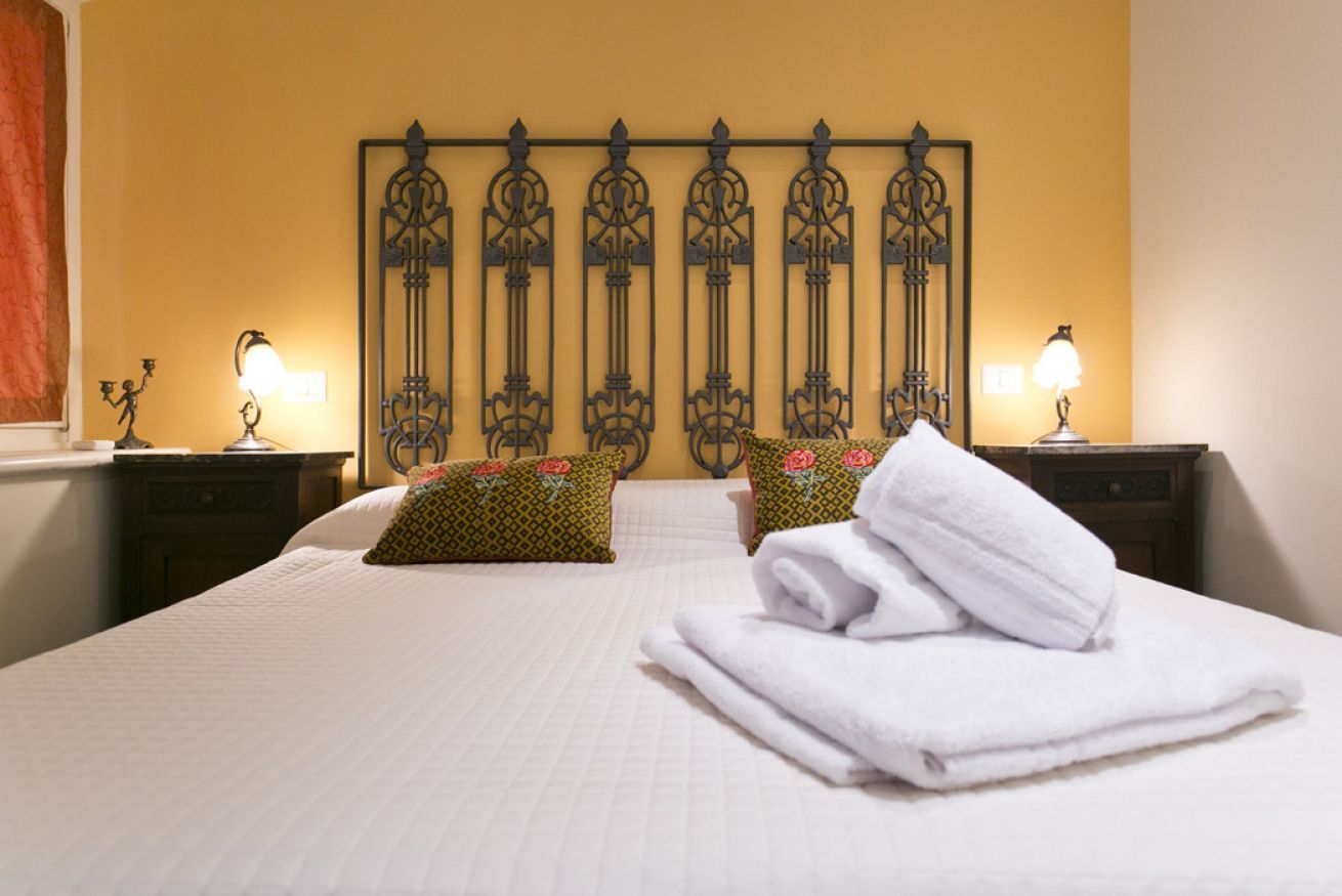 Ein ordentlich bezogenes Bett mit weißen Laken und zwei Kissen, ein dekoratives Wandbild darüber und zwei Nachttischlampen auf den Nachttischen.