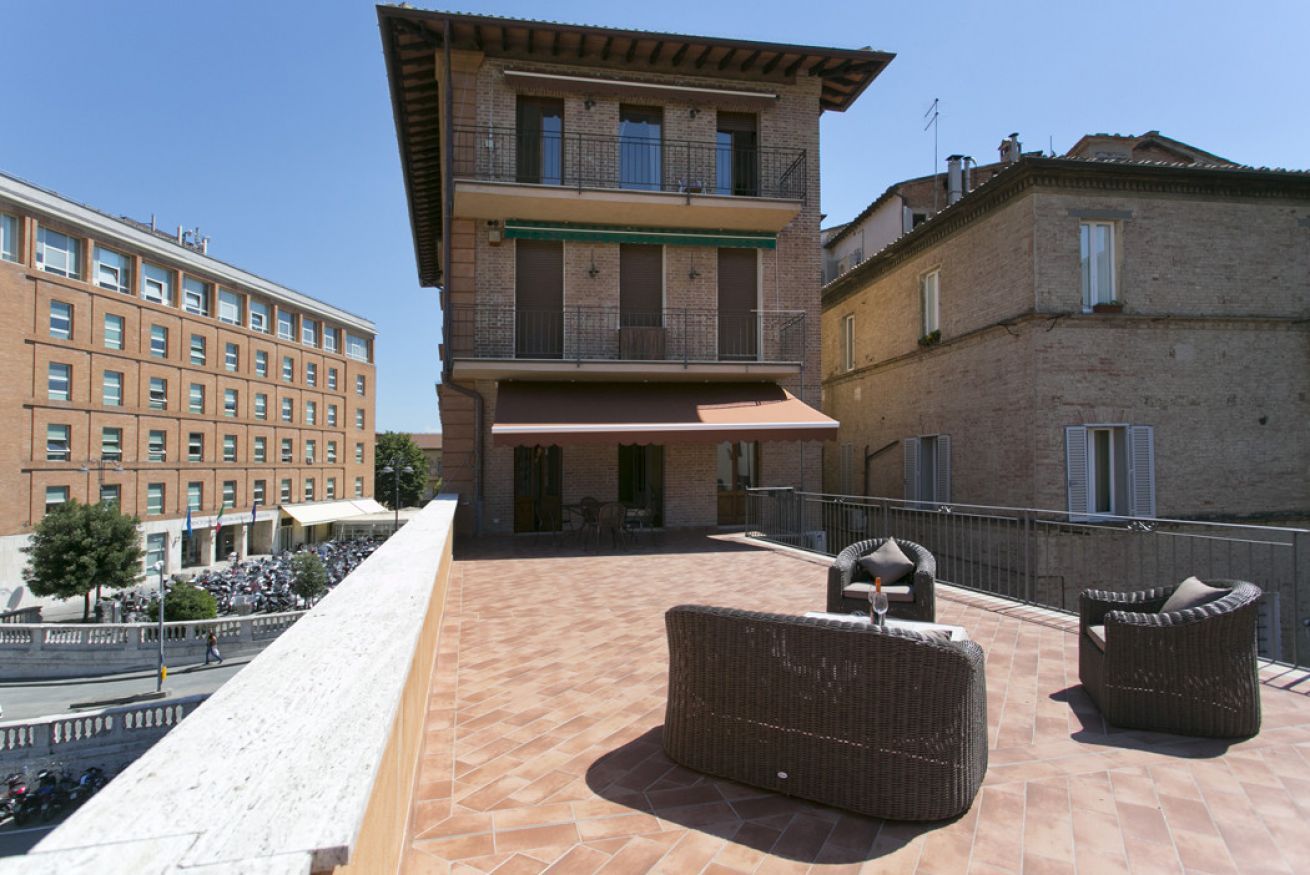 A rooftop terrace with wicker furniture and a view of surrounding buildings.
