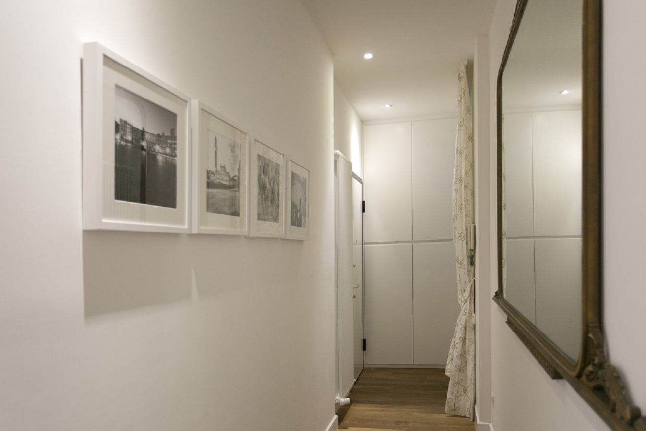 Ein Flur mit Holzboden, weißen Wänden und einer Tür am Ende. An der Wand hängen drei Bilder in Rahmen.