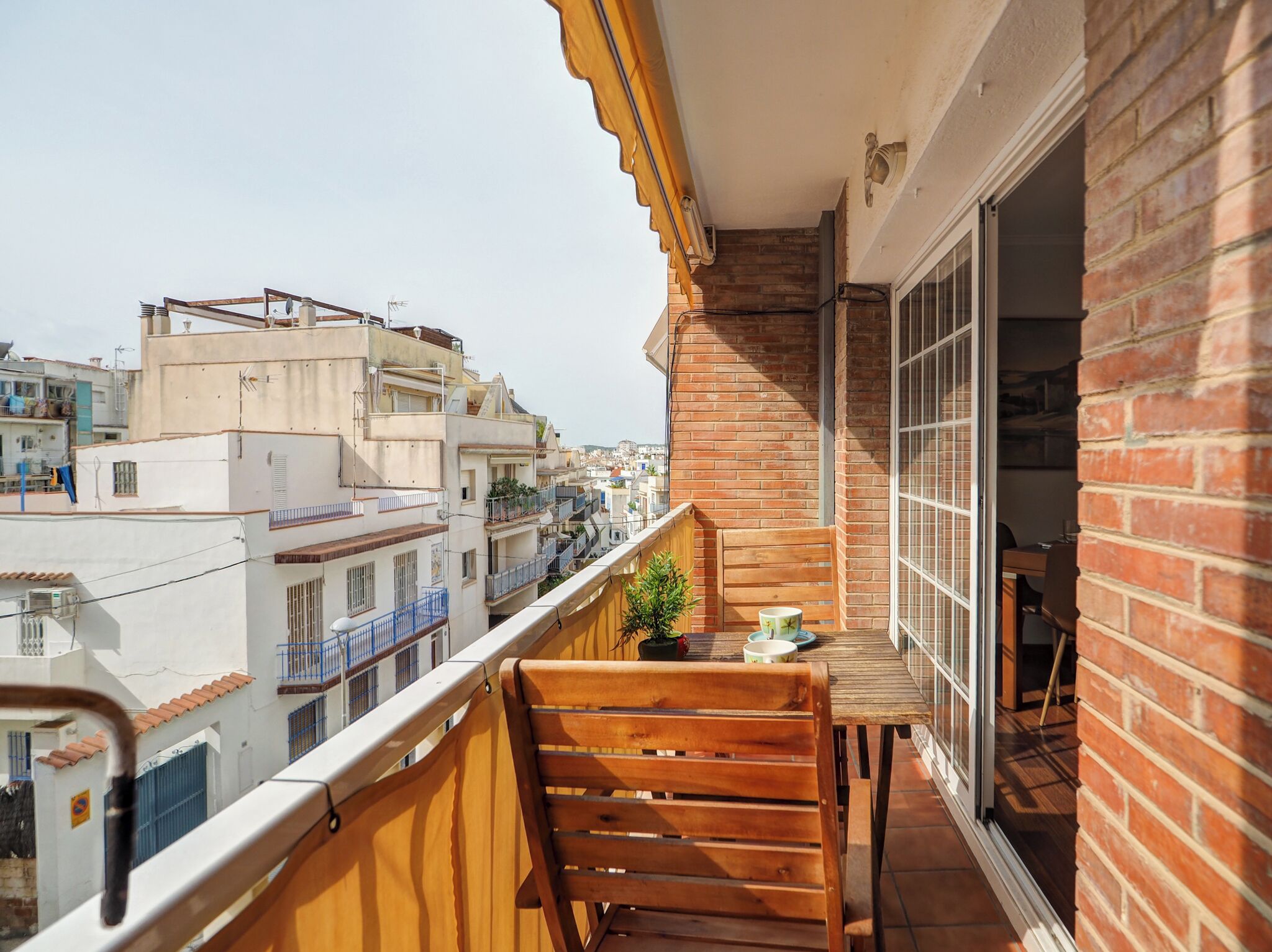 Un balcon avec une chaise en bois, une petite table et un pot de fleurs.