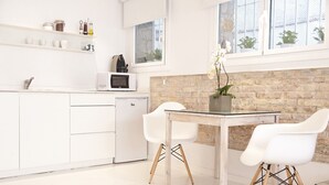 A modern kitchen with white cabinetry, a built-in microwave, and a glass dining table with two white chairs.