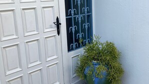 A white door with a blue window, a potted plant, and a wall-mounted lantern.