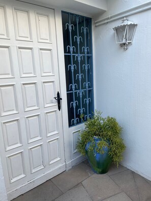 Una puerta blanca con un ventanal azul, una planta en maceta y un farol de pared.