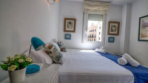 A hotel room with a bed, a desk with a lamp, a potted plant, and two framed pictures on the wall. - The Rose by Hello Homes Sitges (Sitges)