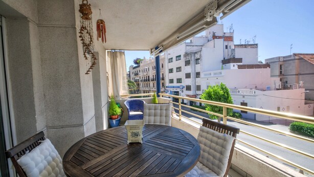 A balcony with a round wooden table, two cushioned chairs, and a hanging decorative item. - The Rose by Hello Homes Sitges (Sitges)