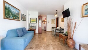 Una sala de estar con un sofá azul, una mesa de comedor con sillas, un televisor montado en la pared y una chimenea.