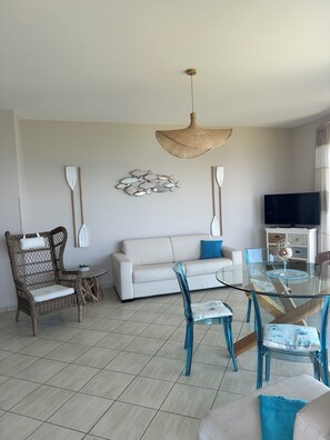 A living room with a sofa, a dining table with chairs, a TV, and a hanging light fixture.