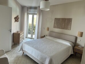 Quarto com cama, penteadeira, mesa de cabeceira, luminária e ar condicionado fixado na parede.