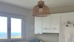 A modern kitchen with white cabinets, a built-in gas stove, a Samsung refrigerator, a window with a view, and a wicker pendant light. - Sea view villa with pool near Tropea (Zambrone)
