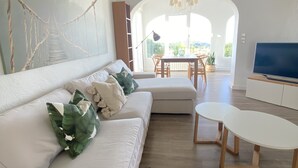 Un salon moderne avec un canapé blanc, un coin repas et un téléviseur.