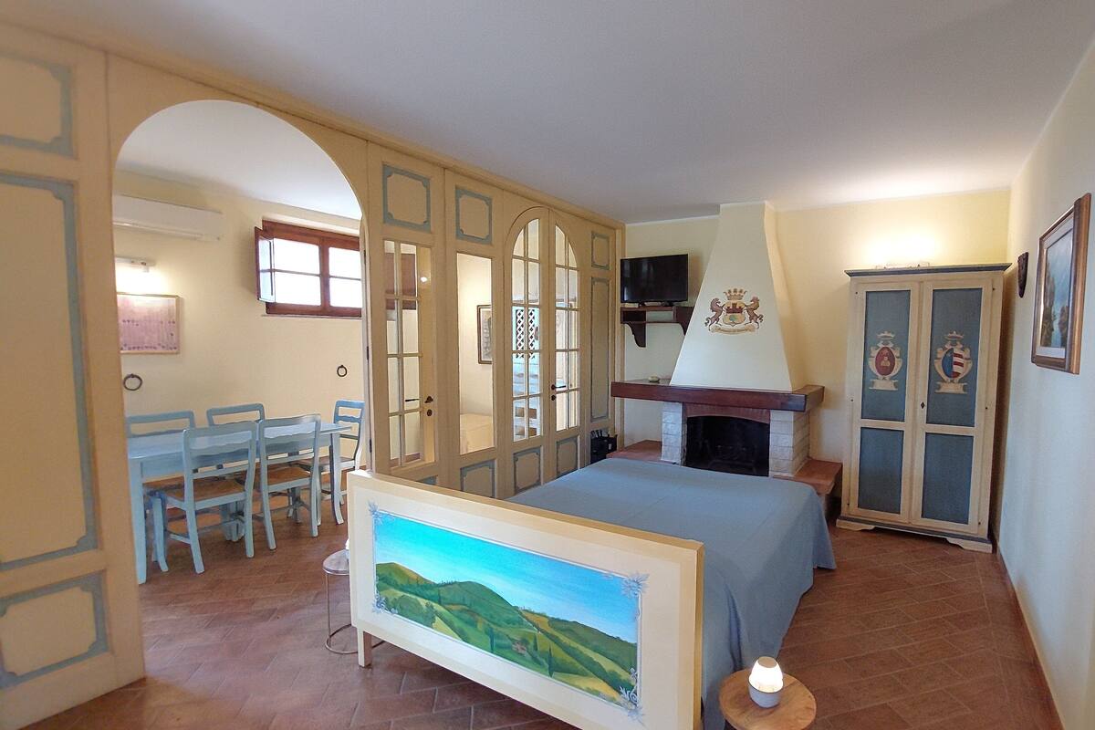 Ein Schlafzimmer mit Bett, einem Gemälde, einem Fernseher, einem Kamin und einem Essbereich mit Stühlen und Tisch.