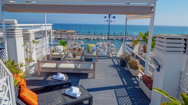 Une terrasse sur le toit avec des sièges extérieurs, une vue sur le port de plaisance et un espace piscine.