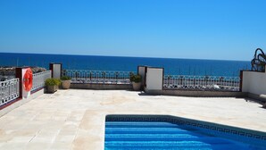 Une piscine sur le toit offrant une vue dégagée sur la mer, une bouée de sauvetage et des plantes en pot.